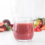 Glass of alive craft smoothie with fruits and vegetables in the background.