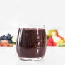 Image of clarity craft smoothie in glass with fruit and vegetables in the background.