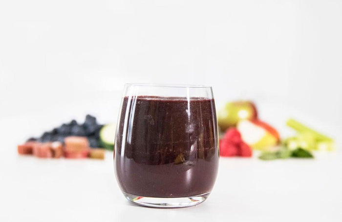 Image of clarity craft smoothie in glass with fruit and vegetables in the background.